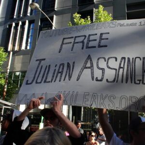 Poster saying Free Julian Assange being held aloft by hands. Its twilight and there are people but no one in full view