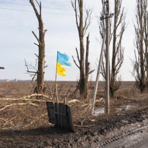 DONETSK REG., UKRAINE - Feb. 14, 2024: War in Ukraine. A torn but proudly flying flag is seen along a road in the Donetsk region, a symbol of an invincible free Ukraine.