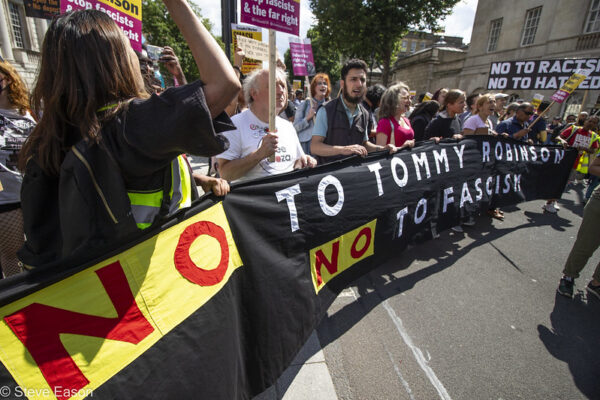 Black banner with No tp Tommy Robinson, No to tascusm with smaller banners in background