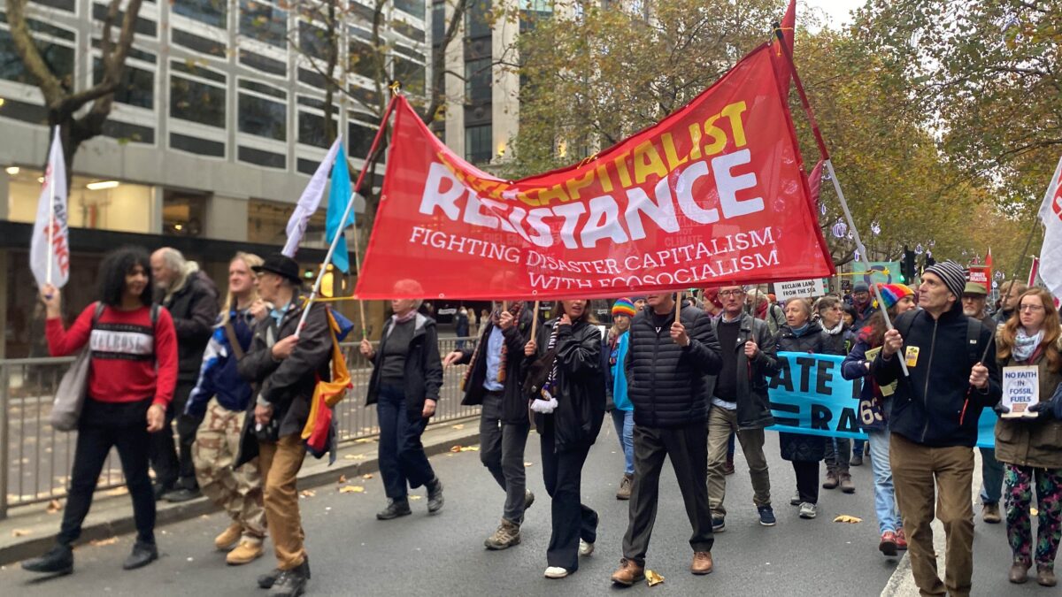 Red Banner with AntiCapitalist Resistance in yellow and white lettering with number of figures carrying it or near it.