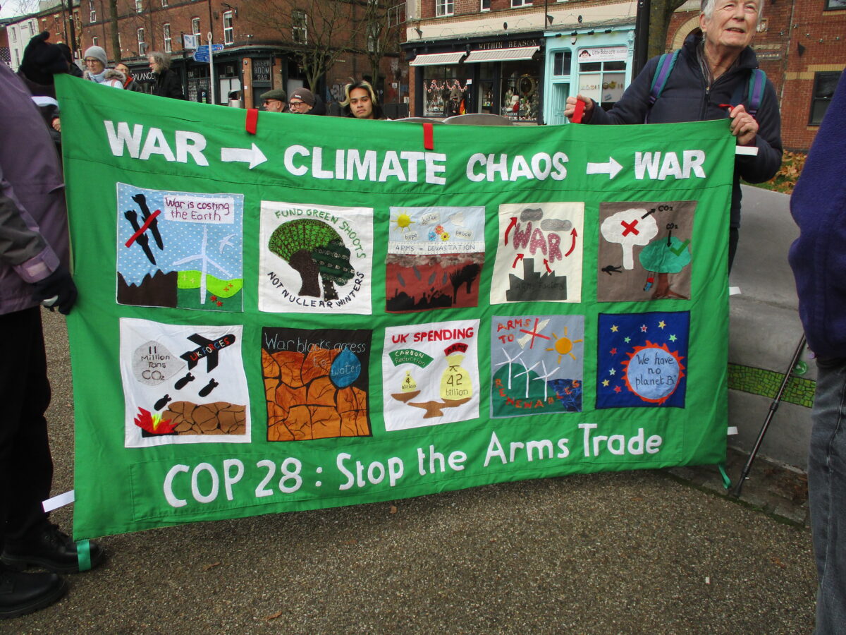 Large banner in Green with number of illustrated panels and the word War -> climate chaos -> War at top and COP 29 End the Arms Trade at the bottom