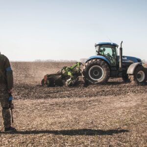 Kyiv, Ukraine - 03 23 2022: Ukrainian soldier of territorial defense looks at the tractor plowing the field during the Russian-Ukrainian war