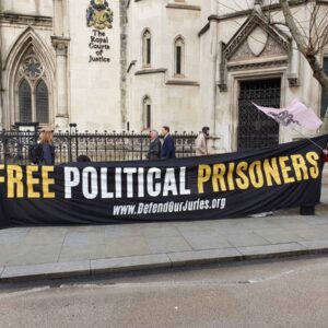 Black Banner with yesllow and White lettering saying: 'Free Political Prisoners www.DefendOurJuries.org' outside Royal Courts of Justice