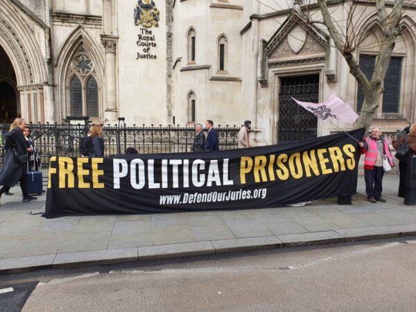 Black Banner with yesllow and White lettering saying: 'Free Political Prisoners www.DefendOurJuries.org' outside Royal Courts of Justice