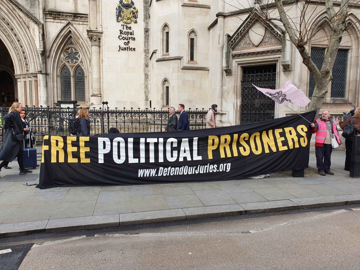 Black Banner with yesllow and White lettering saying: 'Free Political Prisoners www.DefendOurJuries.org' outside Royal Courts of Justice 