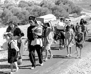 Black and white photo with group of people waking with women carrying children and a cart in background - displaced Palestiian refugees fleeing during the 1948 Nakba