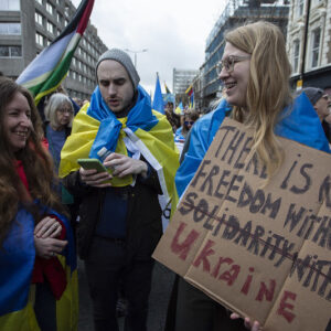 Three figures wearing ukrainian flags one with handmade placard: There is no freedom without solidarity with Ukraine