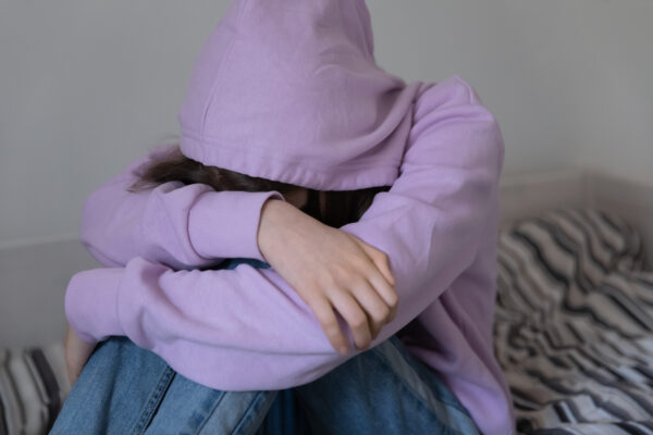 Young person in purple hoodie crouched over hugging their knees so face not visible