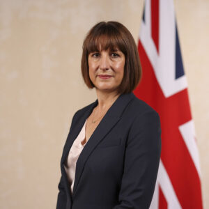 Rachel Reeves standing in front of union jack on flag pole gainst pale background.