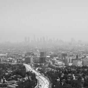Greyscale cityscape of Los Angeles looking out at a foggy horizon with skyscrapers in the background and a road cutting through the middle.