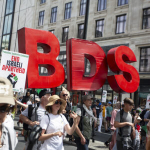 Crowd carrying large red sign BDS
