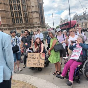Jeremy Corbyn Mp with back to camera addressing a group of protestots with placards. several in wheelchairs