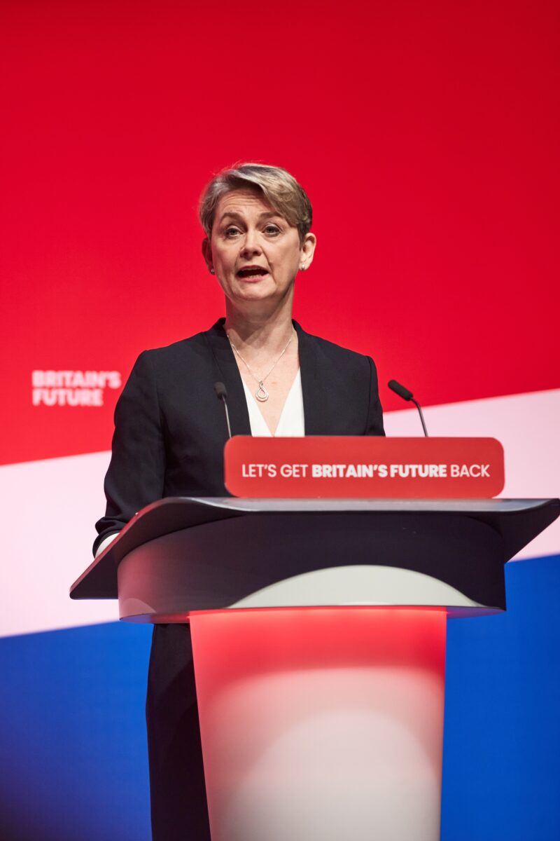 Yvette Cooper at podium with union jack colours behind