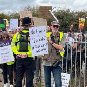 Group of protestors and police. Most prominent protestor holds sign saying No human is illegal.