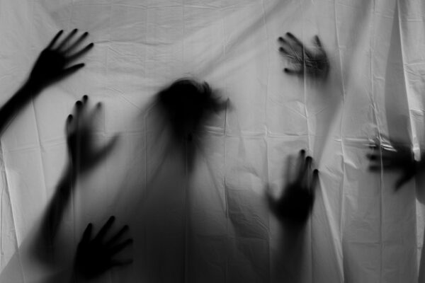 Silhouettes of hands and a head behind a white blanket.
