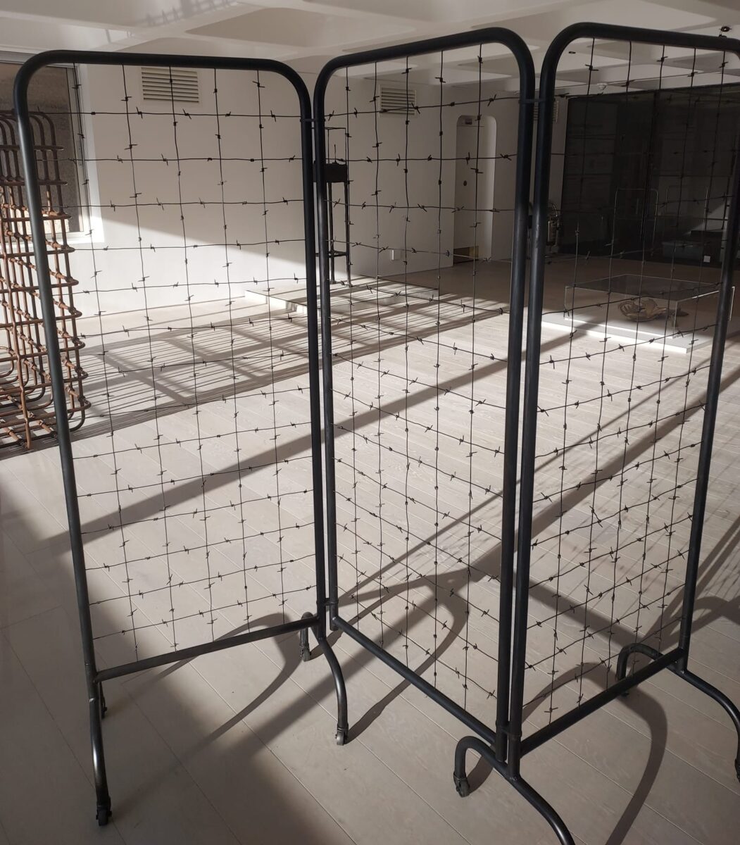 Sculpture of a hospital screen that has a barbed wire mesh rather than curtains