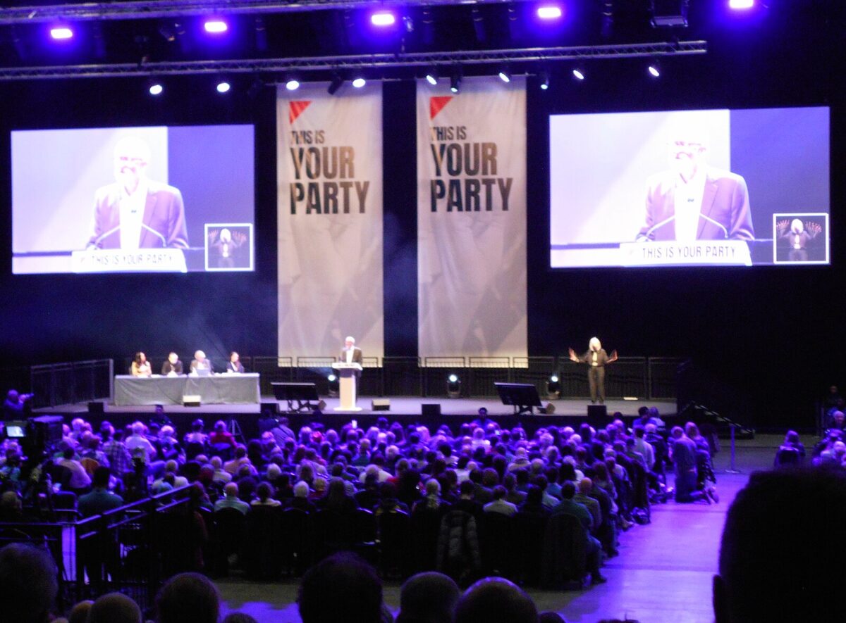 Seats lit in purple, with Your Party banners and large monitors over a stage with podium.
