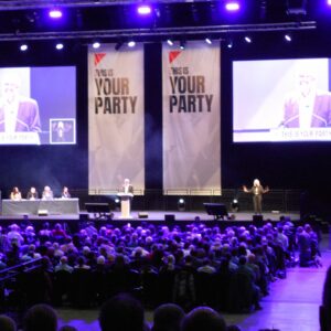 Seats lit in purple, with Your Party banners and large monitors over a stage with podium.