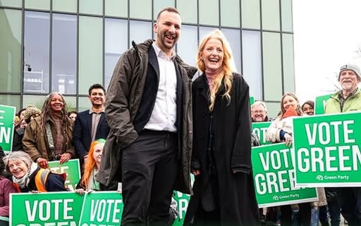 Hannah Spencer and Zack Polansky in front of a crowd holding "Vote Green" placards.