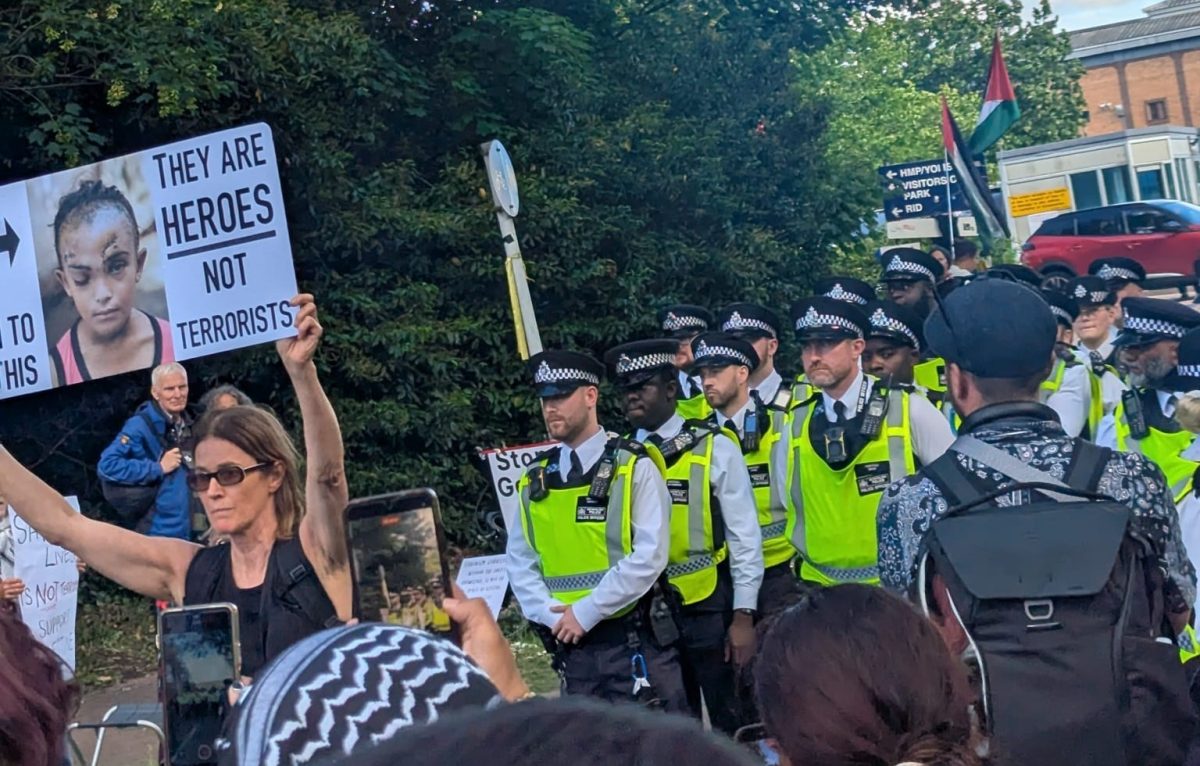 Woman holding a large sign aloft : They are heroes not terrorists with rown of police beside them outside Woolwich Crown Cort 12 June. Photo: Dora Pitura