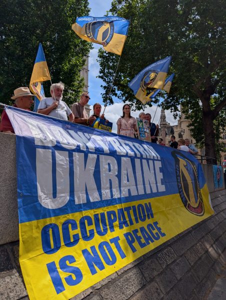 Large blue and yellow banner Dont betray Ukraine: Occupation is not peace surrounded by Ukranian flags