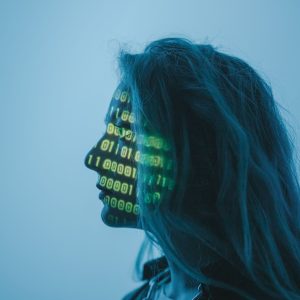 Blue silhouette of a woman with neon green binary code projected on her face.