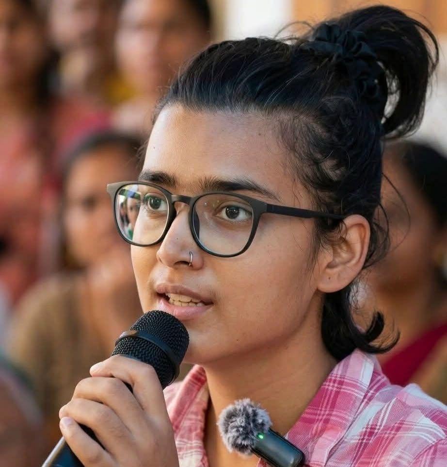 Profile photo of Neda Bora speaking into a mic with a crowd of people in the background. 